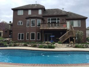 A two-story brown house with a deck and an outdoor pool